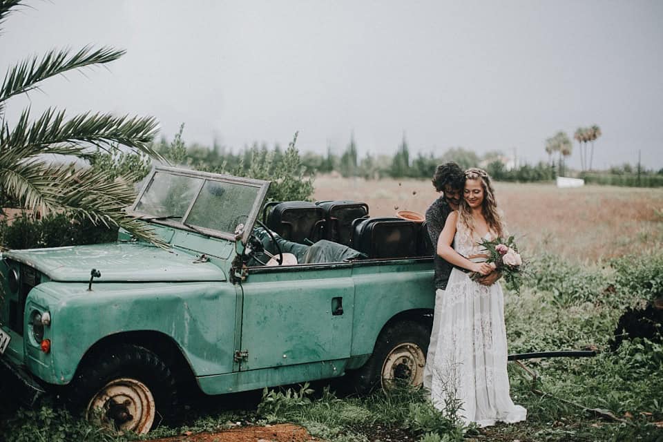 Alter: Romantisches Hochzeitsfoto mit Braut und Bräutigam an einem alten, blauen Land Rover in Naturkulisse.