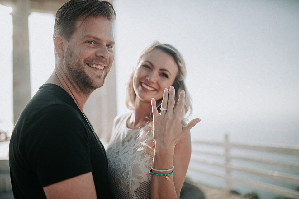 Glückliches Hochzeitspaar zeigt Ehering mit Meerblick im Hintergrund bei Fotografien von Forma Photography.
