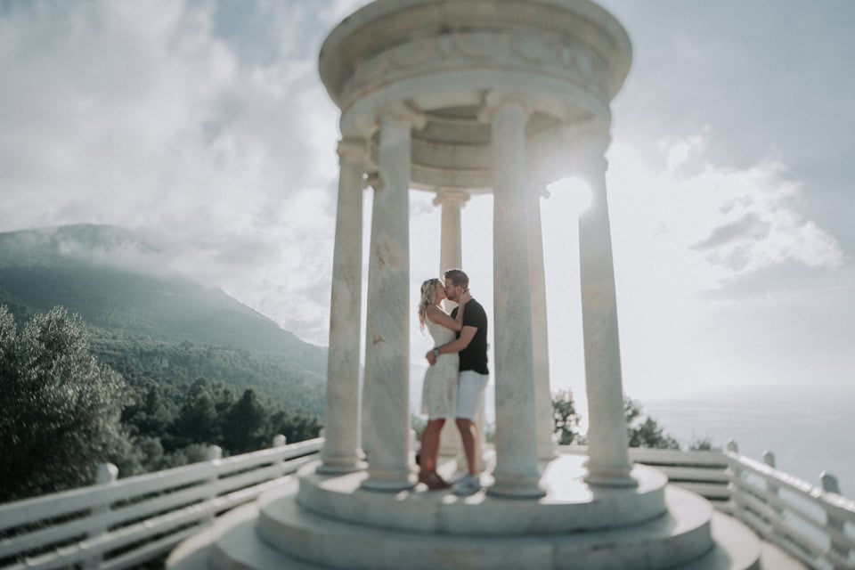 Romantisches Hochzeitsportrait unter einer weißen Pracht auf einer historischen Säule in Tirol, Österreich, mit Bergblick im Hintergrund.