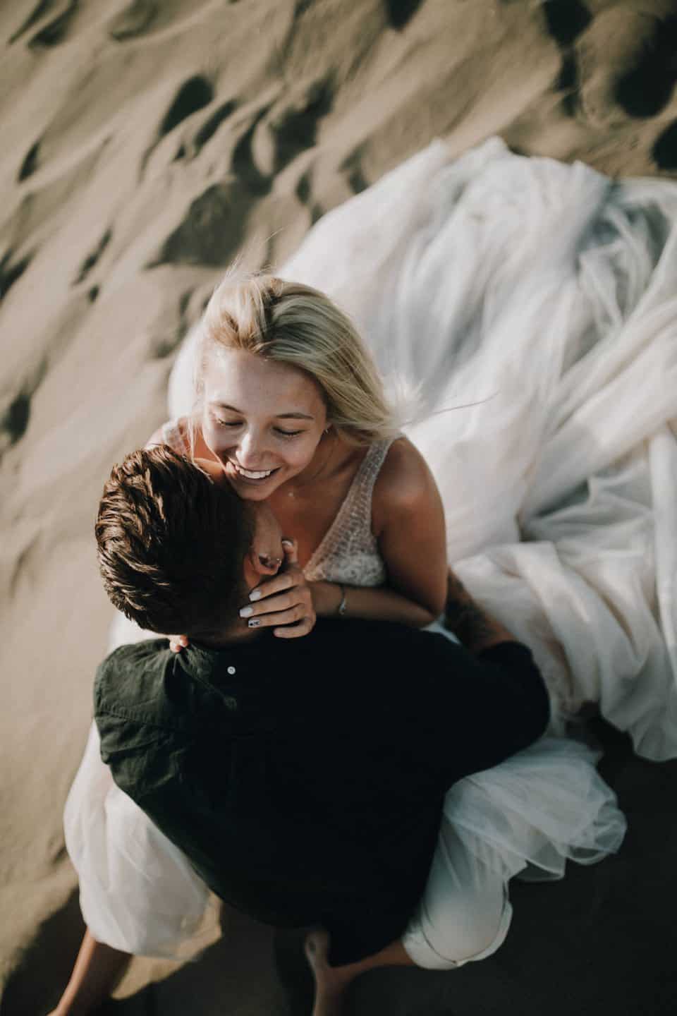 Fröhliches Paar beim Kuscheln auf Sandstrand, romantisches Hochzeitsfoto, Emotionen, Liebe, Natur, Tirol, Österreich, international.