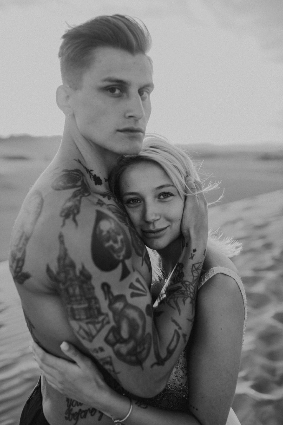 Aufnahme eines jungen Paares am Strand, schwarz-weiß, romantisch, mit Tattoos und Naturhintergrund.