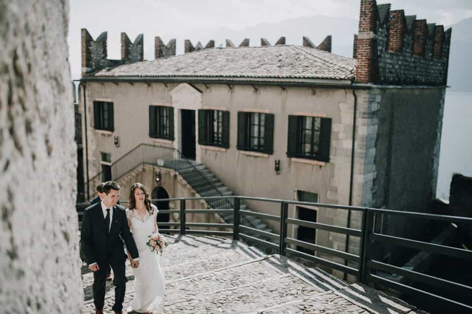Romantisches Brautpaar spaziert in Tirol, Österreich, bei Sonnenlicht auf historischen Gassen.