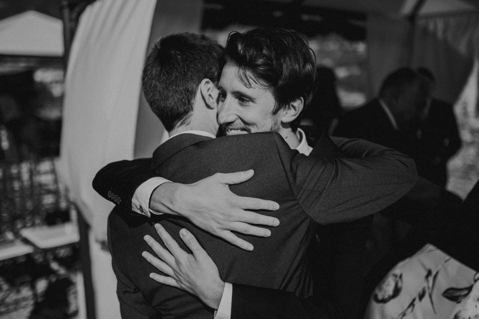 Warmherziges Hochzeitsfoto in Schwarz-Weiß, zwei Männer umarmen sich herzlich.