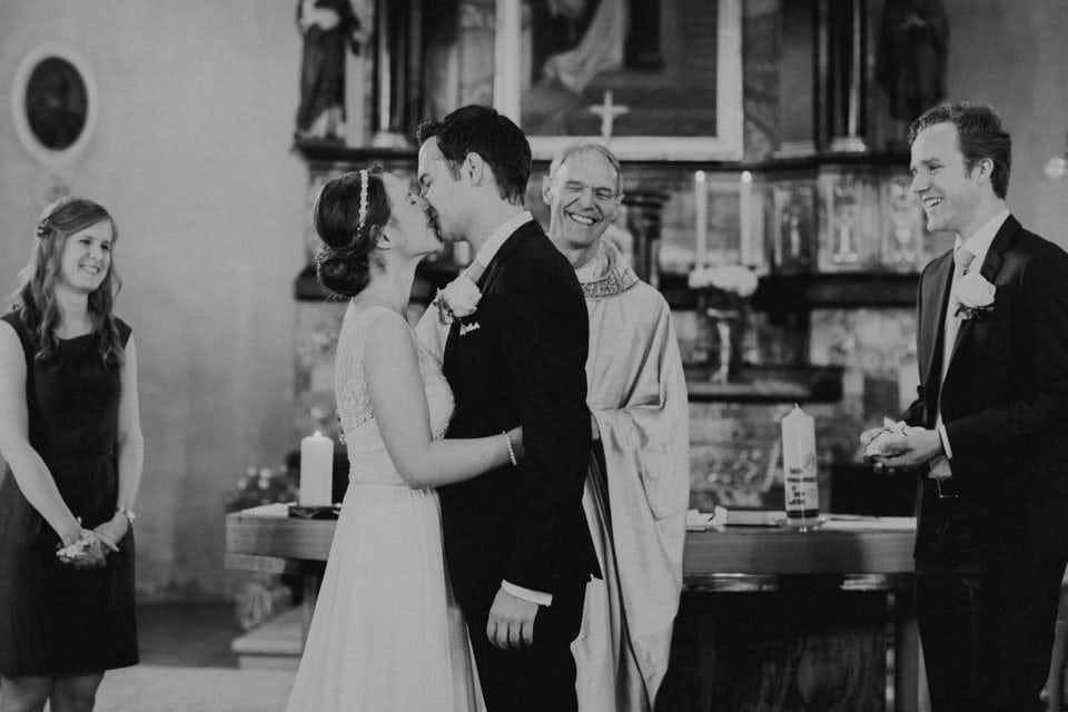 Hochzeitspaar küsst sich in Kirche, Blickwinkel, schwarz-weiß, romantische Atmosphäre.