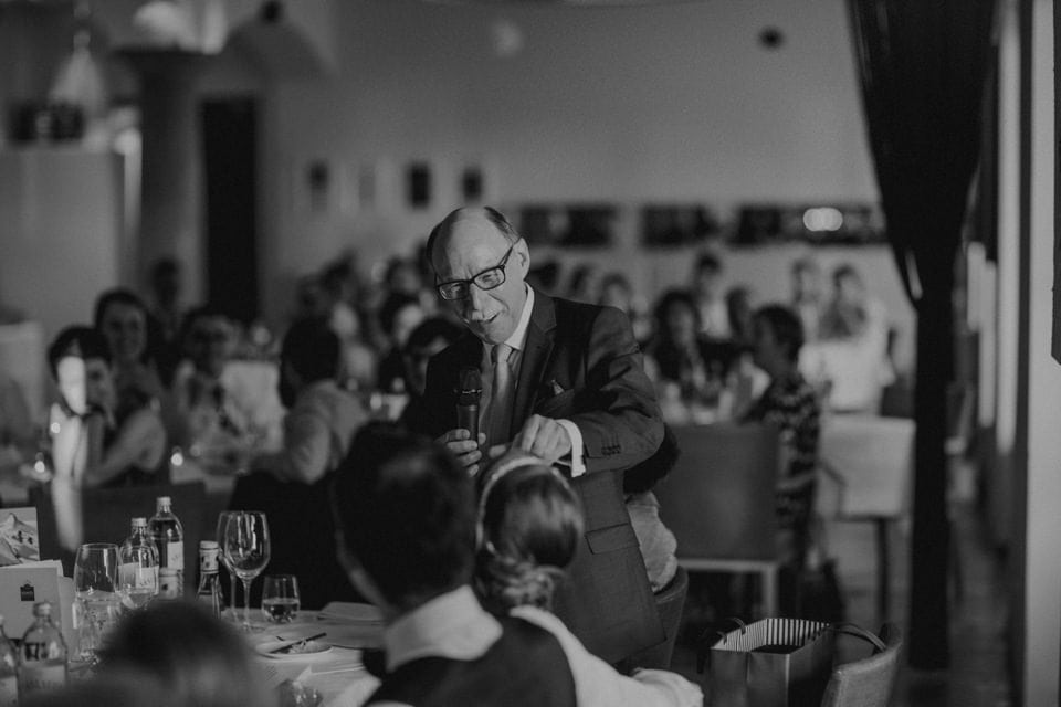 Eleganter Redner bei Hochzeit in Tirol, Österreich, bei emotionaler Ansprache Hochzeitsredner hält bei Feier in Tirol eine Rede vor Gästen Ein Mann in Anzug spricht bei einer Hochzeitsfeier in Tirol in einem Saal mit Gästen, Schwarz-Weiß-Foto Relevanz.