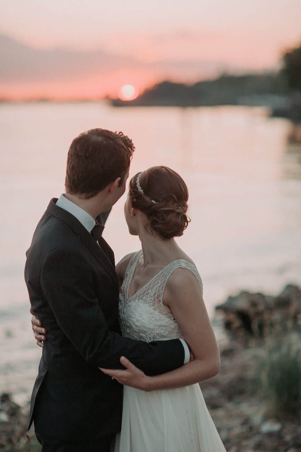 Romantisches Hochzeitsfoto bei Sonnenuntergang am Wasser, verliebtes Brautpaar in Tirol.