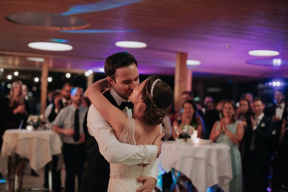 Trauung im rustikalen Hochzeitssaal mit tanzendem Brautpaar und lachenden Gästen, romantische Atmosphäre.