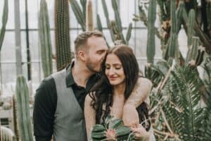 Romantisches Hochzeitspaar umarmt sich in Gewächshaus mit Kakteen, emotionale Hochzeitsfotos in Tirol.