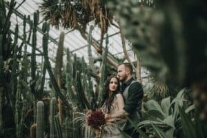 Rauiges, romantisches Hochzeitsfoto in einem Gewächshaus mit dichten Kakteen und exotischen Pflanzen.