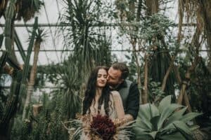 Stilvolle Hochzeitsfotos in einer Gewächshaus-Atmosphäre mit Pflanzen und einem Paar.