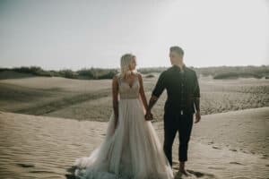 Trauung am Strand mit Braut in weißem Kleid und Bräutigam in dunklem Hemd, romantisches Hochzeitsfoto im Sanddünen-Landschaft.