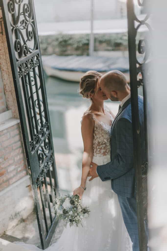 Hochzeitspaar teilt einen Kuss hinter einem schmiedeeisernen Tor mit Blick auf den See.