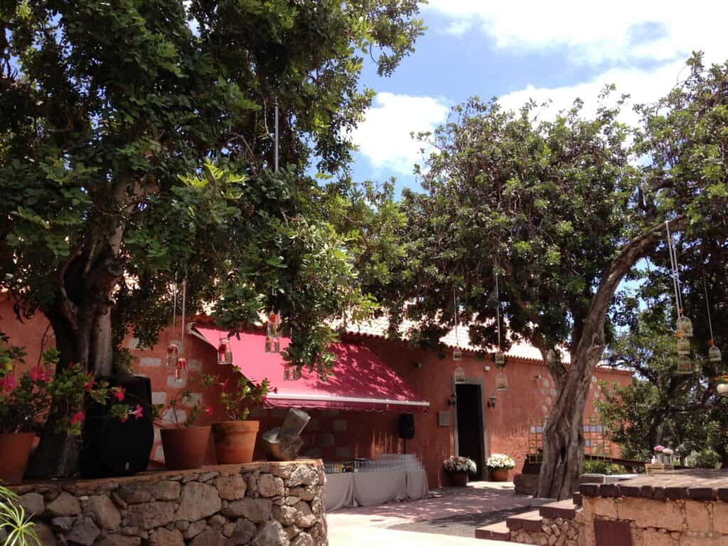 Blumen und Bäume vor einer roten Hausfassade in einer mediterranen Umgebung.