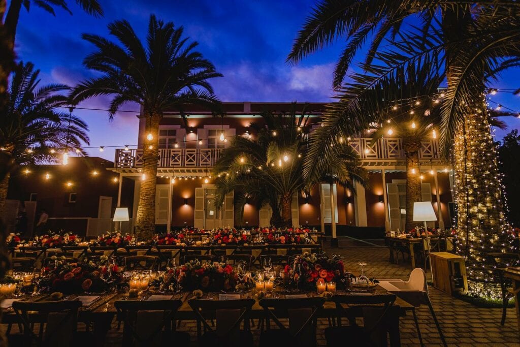 Festliche Hochzeitsfeier im Freien mit Lichterketten und Blumen, romantische Atmosphäre bei Dämmerung.
