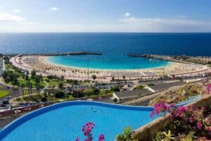 Blick auf eine Strandbucht am Meer mit blauer Wasserfläche und Strandpromenade im Vordergrund, Teneriffa, Kanarische Inseln.