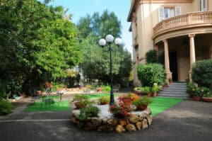 Blumenpavillon im Garten vor einem historischen Haus in Tirol, Österreich, bei Sonnenschein.