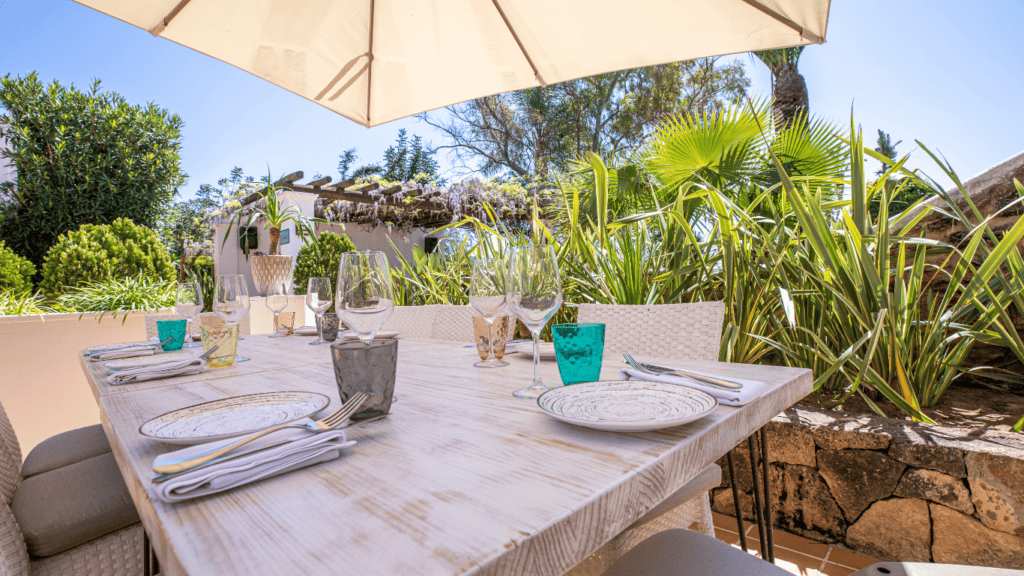 Eleganter Gartentisch im sonnigen Garten mit Geschirr und Glaswaren, ideal für Hochzeiten und Veranstaltungen.