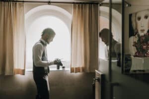 Vorbereitender Bräutigam im Hotelzimmer, Nachdenklich, elegant in Anzug, vor einem Fenster mit natürlichem Licht.