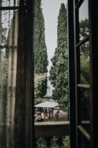 Blumen im Fensterrahmen fotografiert, Blick auf eine ausgelassene Gesellschaft im Garten.