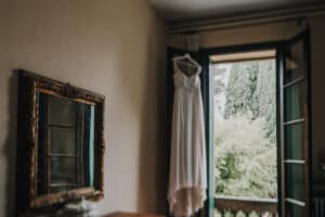 Hochzeitskleid hängt am offenen Fenster mit schöner Naturansicht im Hintergrund.
