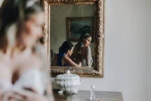 Hochzeitsvorbereitungen: Braut wird von einer Dame im Spiegel für den großen Tag gestylt.