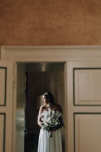 Natürliche Hochzeitsfotografie in Tirol, Braut mit Blumenstrauß blickt nach draußen.