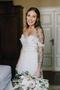 Natürliche Hochzeitsfotografie einer verliebten Braut mit tattoos, Hochzeitskleid und Blumenstrauß bei "Forma Photography" Tirol Österreich.