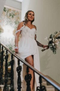 Hochzeitsfotografie: Braut in wunderschönem weißen Kleid auf Treppe mit Blumenstrauß.