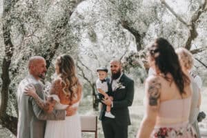 Innenaufnahme von Hochzeitsgästen unter Olivenbäumen in Tirol, Österreich, bei einer emotionalen Zeremonie.