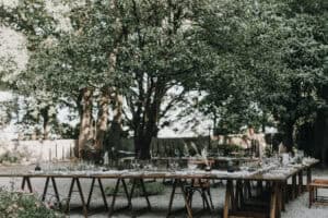 Elegantes Hochzeitsdekoration im Grünen, rustikaler Festsaal im Freien, stilvoll gedeckter Tisch mit Kerzen und Blumen.