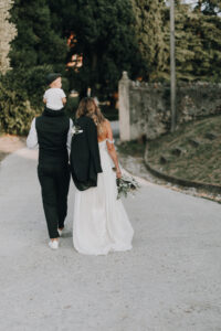 Hochzeitspaar auf Spaziergang bei Sonnenuntergang in Tirol, Österreich, romantisches Brautpaar mit Blumen.