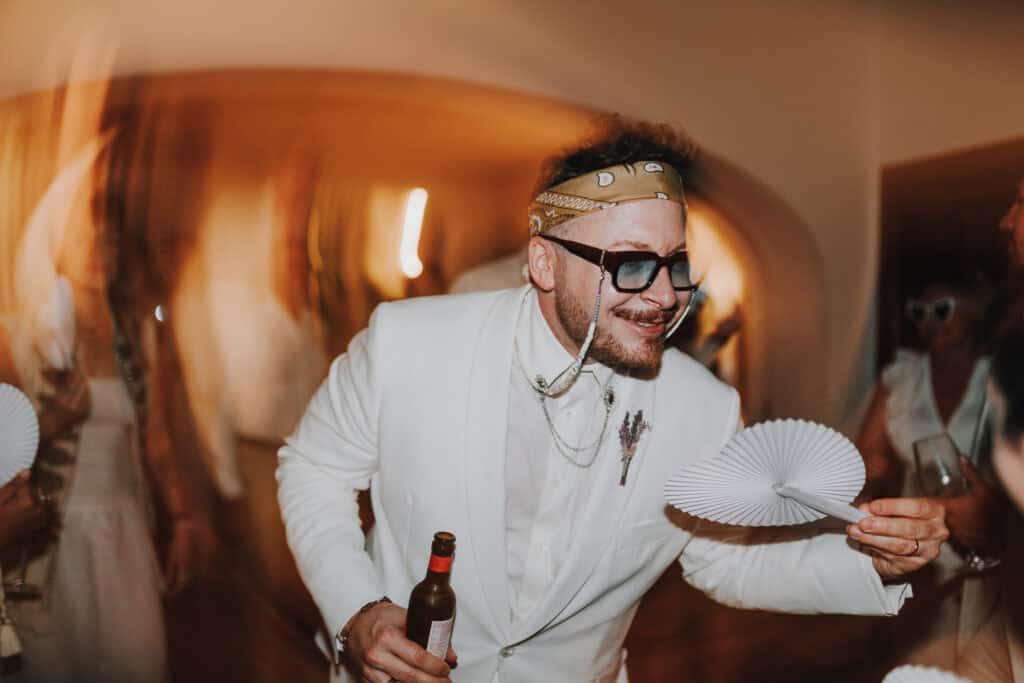 Bräutigam in weißem Anzug mit Fächer und Bier, feiert auf Ibiza.