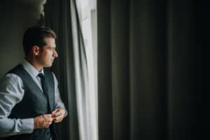 Bräutigam im grauen Anzug blickt aus dem Fenster. Hochzeitsfotograf Irland.