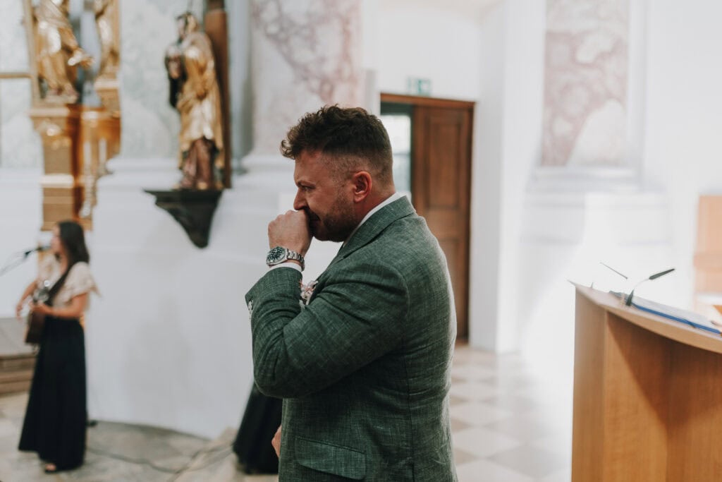 Bräutigam emotional in Kirche mit Musikerin im Hintergrund. Hochzeit in München.