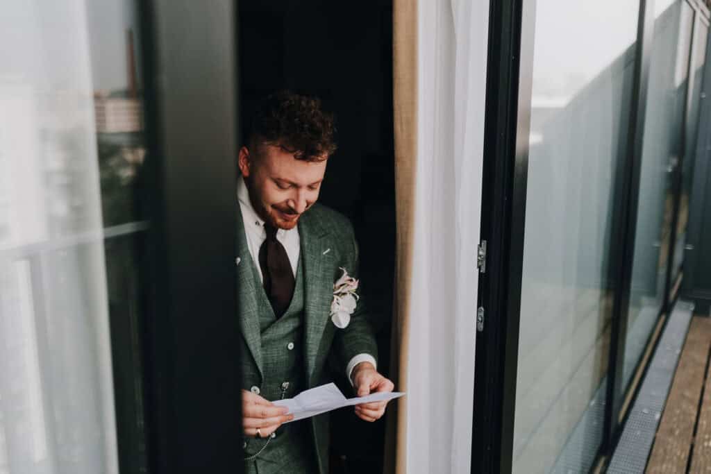 Bräutigam im grünen Anzug liest Brief am Fenster, Hochzeit.