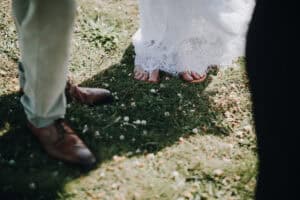 Braut barfuß mit Spitze, Bräutigam mit Lederschuhen im Gras. Hochzeit im Freien.