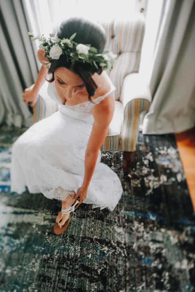 Braut mit Blumenkranz setzt Sandalen an. 