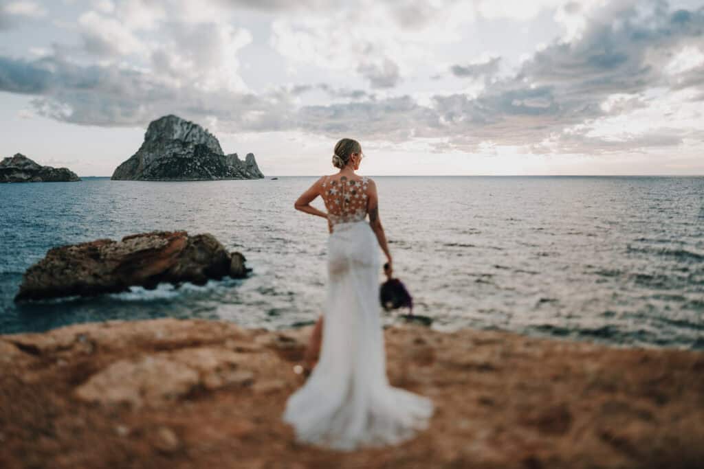 Braut mit Tattoo blickt auf Es Vedrà, Ibiza. Hochzeit auf Ibiza.