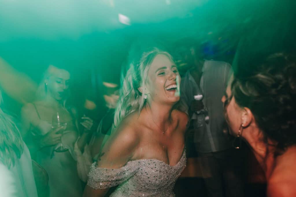 Braut lacht auf der Hochzeitsparty in München, umgeben von Gästen und grünem Licht.