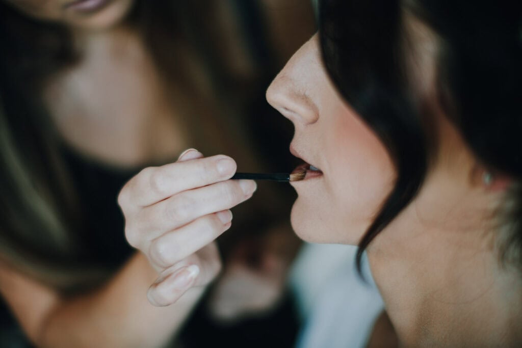 Visagistin trägt Lippenstift auf, Brautstyling. Detailaufnahme vom Schminken.
