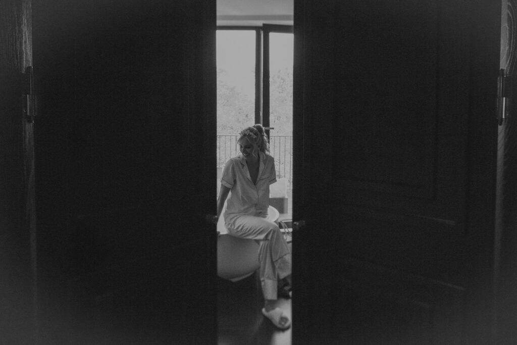 Braut im Pyjama sitzt auf Badewanne vor Fenster. Vorfreude auf Hochzeit in München.