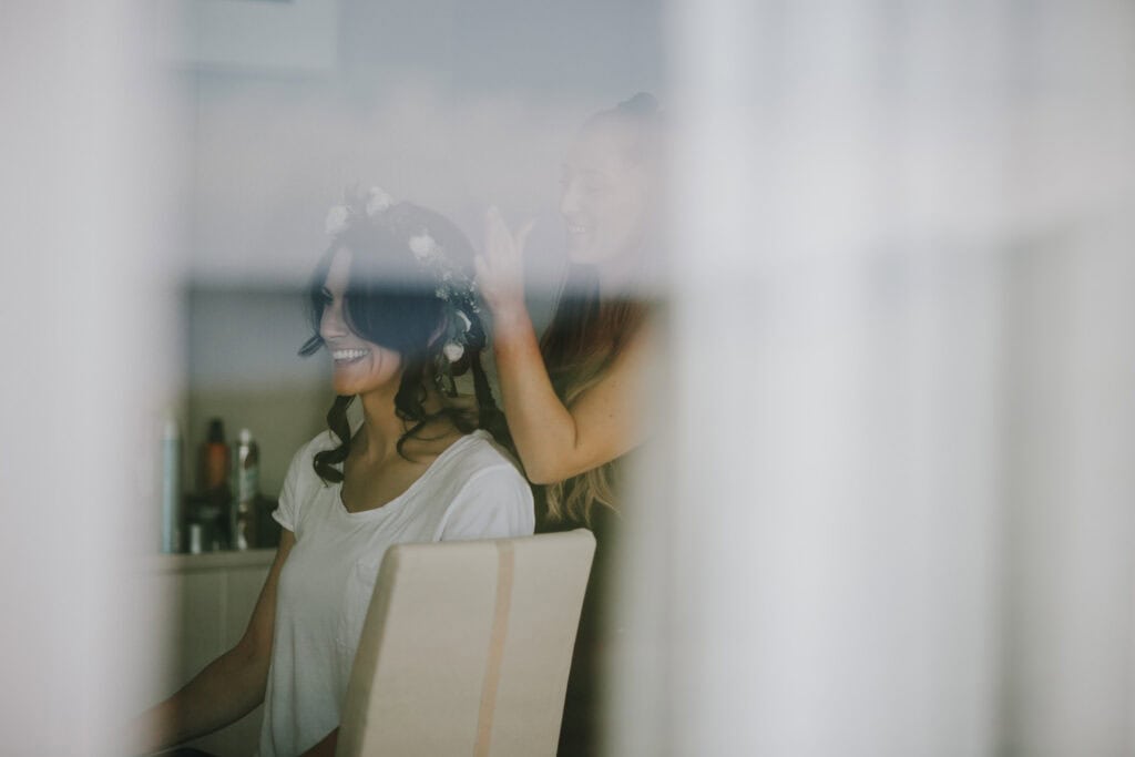 Brautstyling vor der Hochzeit in Irland: Fröhliche Frau mit Blumenkranz bekommt die Haare gemacht.