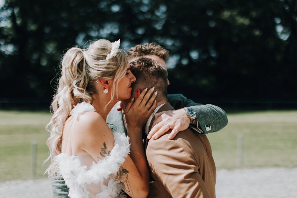Braut umarmt Freunde auf Hochzeit im Freien. Elegante Hochzeitsfrisur, Blumenapplikationen. Herzliche Umarmung.