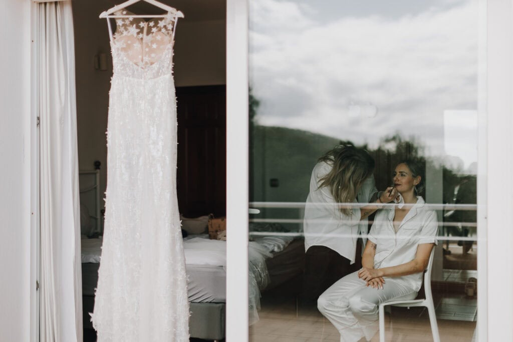 Brautkleid hängt am Fenster, Braut wird geschminkt. Vorbereitung für Hochzeit auf Ibiza.