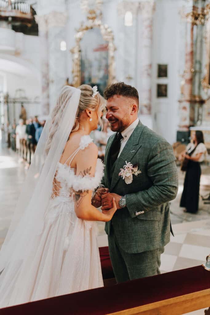 Brautpaar im Gespräch in Kirche. Brautkleid mit Federn, Bräutigam im Anzug. Hochzeit München.