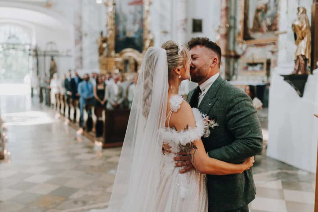 Brautpaar küsst sich in Kirche, Hochzeitsfotograf München. Festliche Hochzeitszeremonie.