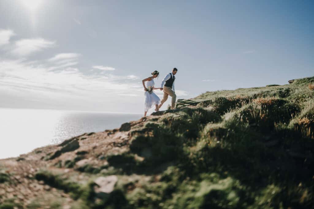Brautpaar läuft Hand in Hand auf einer Klippe in Irland. Küste im Hintergrund. Hochzeitsfotograf Irland.