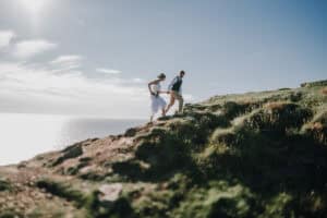 Brautpaar läuft Hand in Hand auf einer Klippe in Irland. Küste im Hintergrund. Hochzeitsfotograf Irland.