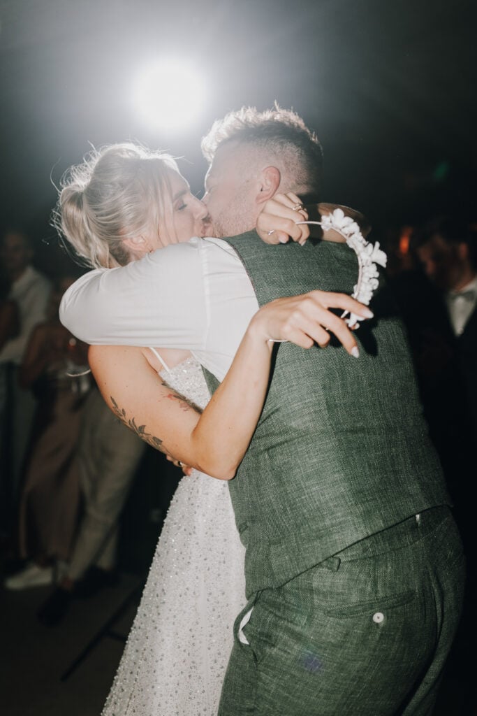 Brautpaar umarmt sich und küsst sich innig bei der Hochzeit. Braut hält Blumenkranz in der Hand.