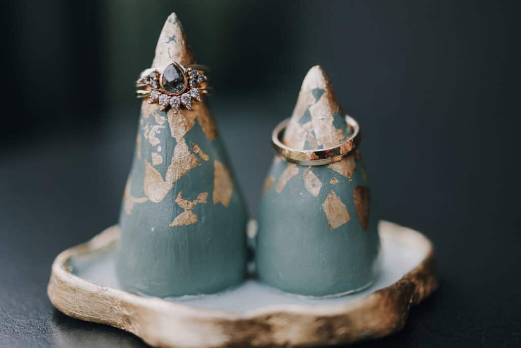 Eheringe auf blau-goldenen Schmuckhaltern. Goldener Ehering und Ring mit dunklem Stein. Hochzeitsschmuck.